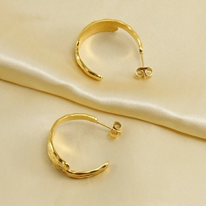 Golden geometric textured earrings on beige silk fabric with natural soft lighting