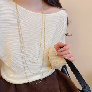 Macro detail of triple-layer gold necklace with fine metallic beads on minimal chains