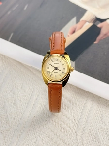 Close-up of a women's quartz watch with a gold case and brown leather strap on white fabric