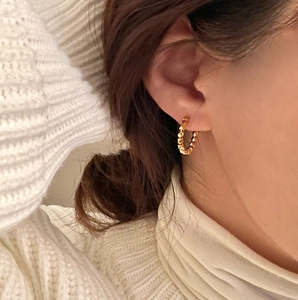 Close-up of heart-shaped faceted gold hoop earrings worn on a warm beige knit sweater