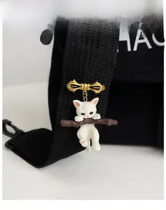 Detail of white resin cat hugging a branch attached to a golden bowknot brooch