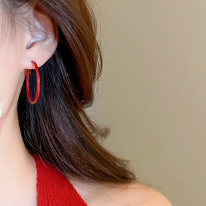 Close-up of minimalist glossy red hoop earrings worn by a model for a chic fall look