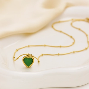 Detail of vintage gold snake chain with green heart pendant on a ceramic plate