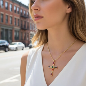 Dettaglio di una collana a croce dorata con gemme multicolori indossata da una modella