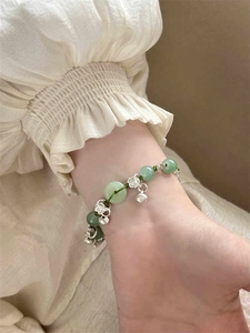Detail of green beaded bamboo bracelet with silver rose, bell and money bag charms on wrist