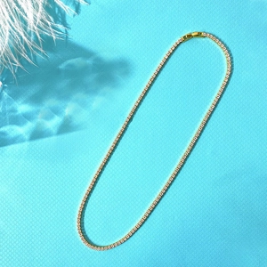 Close-up of golden tennis necklace with 2mm white zircon stones on blue background