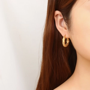 Close-up of golden C-shaped hoop earrings with hammered texture on a female model