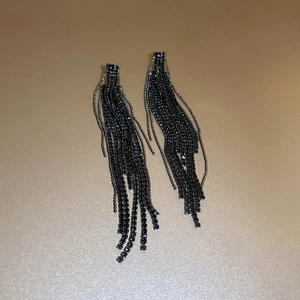 Close-up of long black tassel earrings with sparkling rhinestones on a golden surface