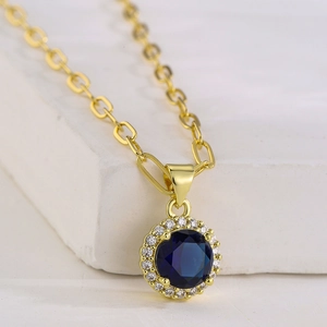 Collana placcata oro 18K con gemma blu e zirconi su sfondo in pietra bianca naturale