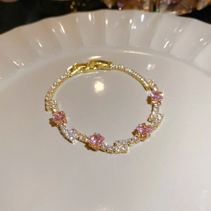 Close-up of gold tone bracelet featuring pink square cut stones and clear pavé zircons