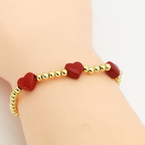 Detail of beaded bracelet with golden beads and red heart charms on a wrist