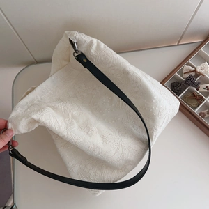 Detail view of beige cotton tote bag featuring floral lace embroidery and black leather strap