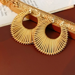 Detail of gold hollow circular earrings with textured radial lines on red leather background