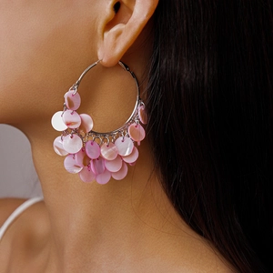 Close-up of pink shell disc tassels on silver hoop earrings worn by a model