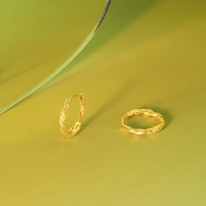 Detailed view of twisted gold hoop earrings with braided texture on a gradient background