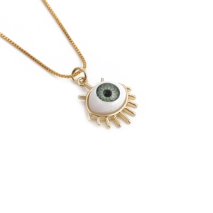 Close-up of golden evil eye pendant with green iris and decorative eyelashes on box chain