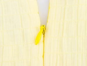Close-up of a yellow dress showing textured fabric detail and a concealed zipper