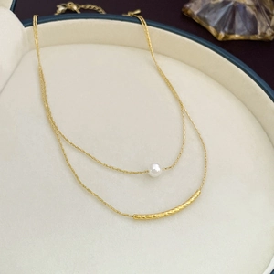 Detail of double-layer gold necklace featuring a white pearl and textured curved pendant