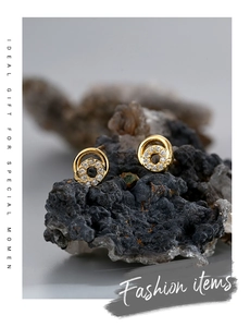 Macro detail of gold-plated circular stud earrings with pavé zircons on a dark stone