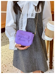 Detail of bright purple crossbody bag with large bow and gold chain on model