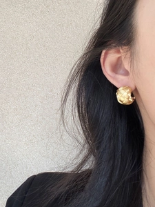 Close-up of golden woven texture spherical earring worn by a model in a warm setting