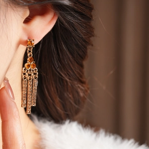 Close-up of vintage golden fringe earrings with orange gems and shimmering crystals