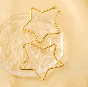 Gros plan de boucles d'oreilles étoiles dorées en acier sur plateau en verre