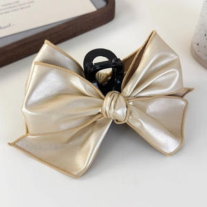 Close-up of a large gold faux leather bow hair claw clip with detailed beige stitching