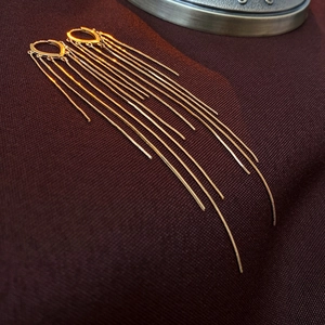 Vue détaillée des boucles d'oreilles pendantes à pampilles dorées sur fond texturé