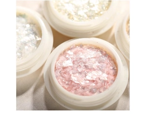 Close-up of aurora opal nail powder and iridescent pink silver glitter flakes in a small jar