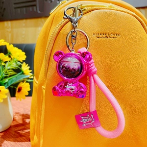 Vibrant pink electroplated space bear keychain hanging on a bright yellow backpack
