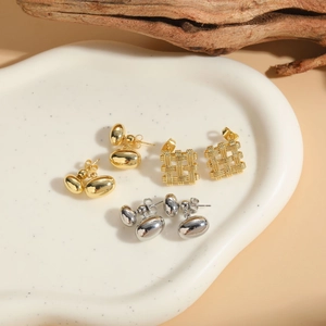 Close-up of geometric square woven and oval metal stud earrings on a ceramic tray