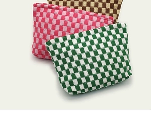 Close-up of three knitted checkerboard makeup bags in green, pink, and brown with zippers
