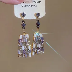 Orecchini pendenti dorati con cristalli viola e bianchi presentati su cartoncino moda