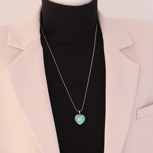 Close-up of golden heart pendant with turquoise devil eye on model wearing a beige blazer