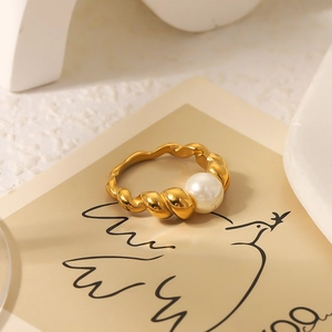 Elegant gold twisted stainless steel ring with white pearl detail on minimalist paper