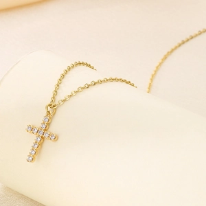 Polished gold stainless steel cross necklace with cubic zirconia on a jewelry stand