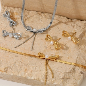 Elegant gold and silver bow jewelry set with pearls on stone background