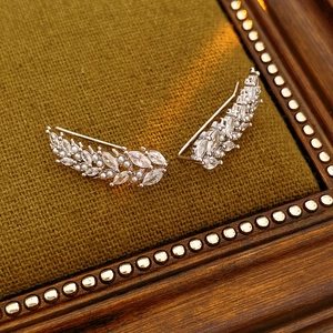 Detailed view of silver wheat ear earrings with zircon and pearls on green fabric