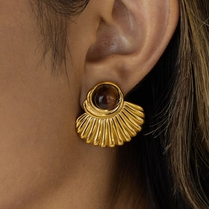 Close-up van een gouden waaiervormige oorbel met tijgeroog gedragen door model