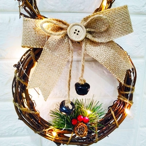 Christmas wreath with LED lights, burlap bow, pine cones, and berries on white wall