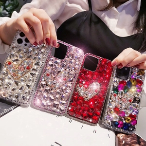 Close-up of four luxury rhinestone iPhone cases with heart designs held by a hand