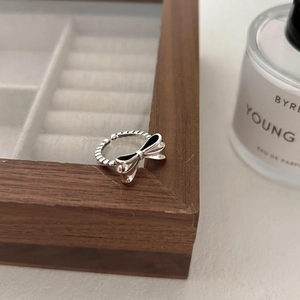 Adjustable 925 sterling silver bow ring with black enamel accent on a wooden jewelry box