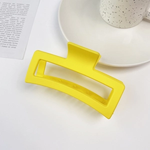 Detail of a large 13cm matte yellow square shark hair claw clip on a stylish desk setting