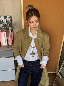 Close-up of a large vintage metal cross pendant necklace styled on a khaki trench coat outfit
