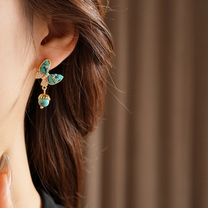 Gros plan sur boucle d'oreille papillon dorée avec turquoise sur l'oreille
