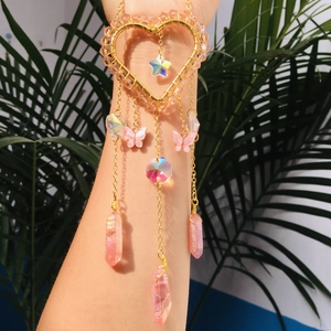 Macro detail of a golden heart bracelet featuring pink and iridescent crystal pendants
