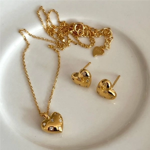 Close-up of gold heart jewelry set with white zircons and S925 stamp in a ceramic tray