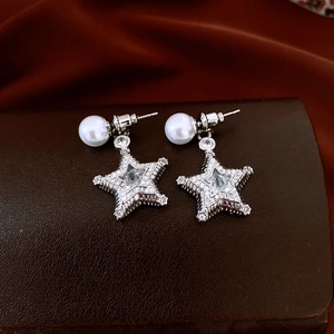 Macro shot of star earrings with sparkling zircon inlay and pearl detail on brown leather