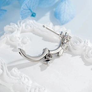Silver star pendant hoop earring with bow design and small crystals on white surface